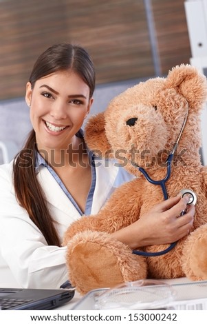 Laughing doctor examining teddy bear with stethoscope.
