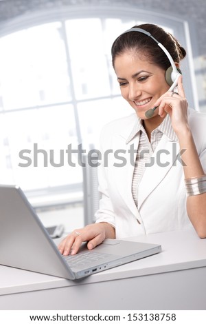 Dedicated customer service representative working on laptop computer, using headset, smiling.