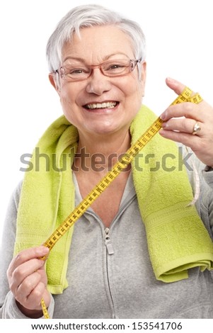 Happy old lady holding tape measure, towel around neck, smiling.