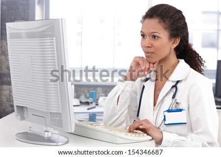 Afro-american female doctor sitting at desk working on computer.