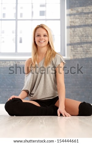 Attractive young female dancer sitting on floor in practice room, smiling happy.