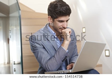 Young businessman sitting on stairs at home, using laptop computer, working.