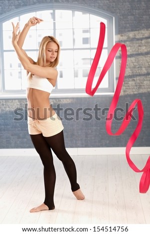 Pretty young rhytmic gymnast exercising with ribbon in exercise room.