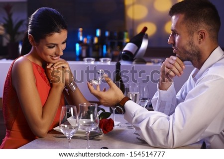 Young man proposing to beautiful woman, holding engagement ring, waiting for answer.