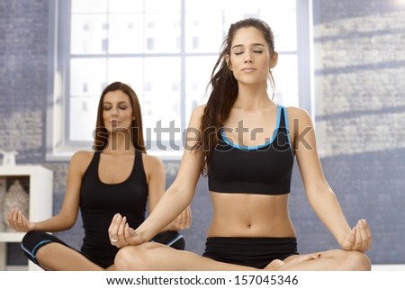Attractive young women sitting in tailor seat eyes closed, practicing yoga, meditating.