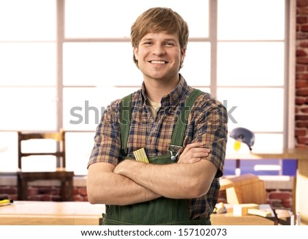 Happy young handyman carpenter in workshop, smiling.