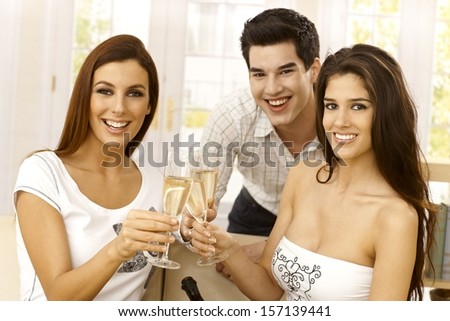 Closeup portrait of happy young people clinking with champagne flute, smiling, looking at camera.