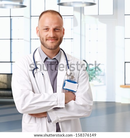 Portrait of young caucasian doctor at clinic waiting room, smiling.