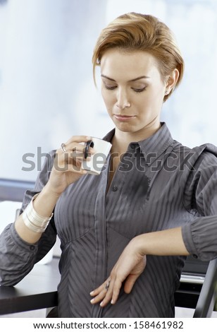 Young businesswoman looking at stain on her blouse made by spilling coffee on it.