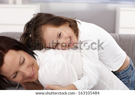 Happy little girl hugging mother from behind, both smiling.
