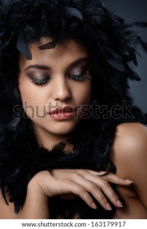 Beauty posing with black feather boa, extravagant eye makeup.