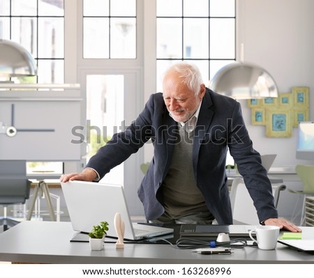 Senior Architect Standing By Desk Working With Computer At Office.
