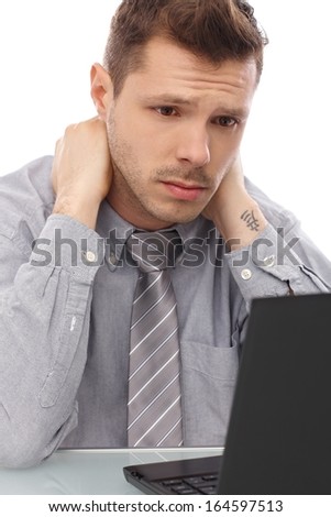 Tired, troubled businessman sitting at desk, working on laptop computer.