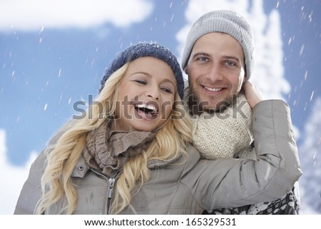 Happy loving couple laughing, embracing, having fun in snowfall.
