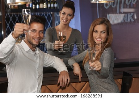 Young couple and waitress drinking champagne, lifting glasses, smiling happy in bar.