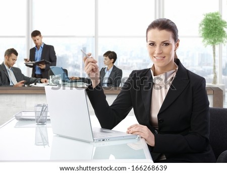 Middle-aged businesswoman with laptop at office desk, smiling.