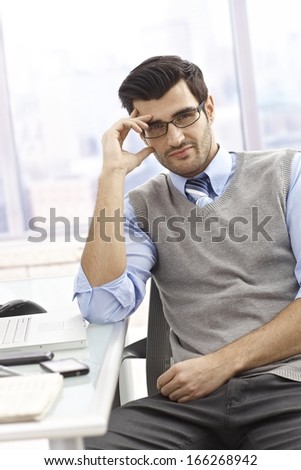 Portrait of casual office worker sitting at desk in bright office, smiling.