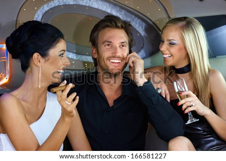 Happy young people having fun in luxury car, drinking, smoking cigar.