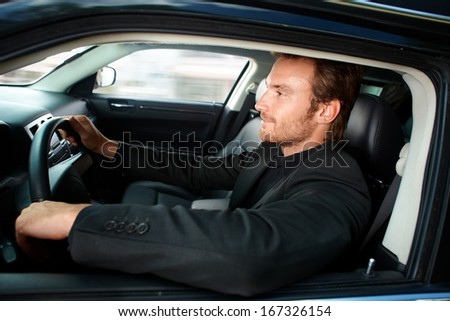 Young man in black driving luxury car, smiling.