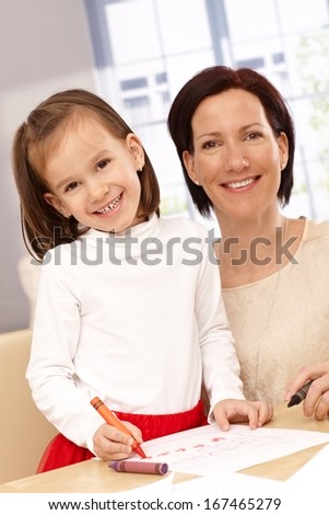 Portrait of happy mother and little daughter drawing.