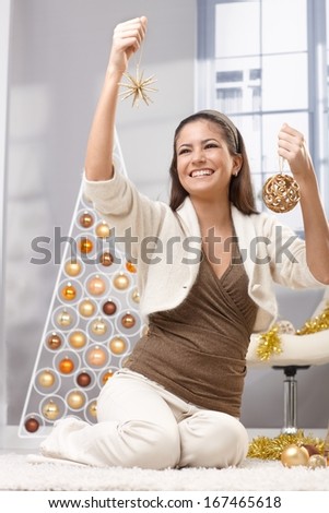 Happy pretty woman decorating for christmas, holding bulb and star, laughing, sitting in festive living room.