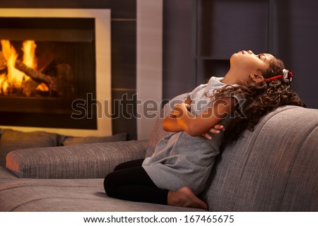 Little ethnic girl sulking on sofa, kneeling, arms crossed.
