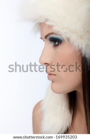 Beautiful female profile in white fur cap and professional makeup.