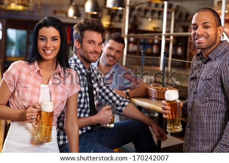 Happy young people drinking beer in pub, smiling.