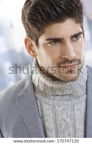 Closeup portrait of handsome young man in polo-neck sweater, looking away.