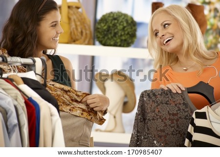 Female friends shopping together at clothes store, smiling happy.