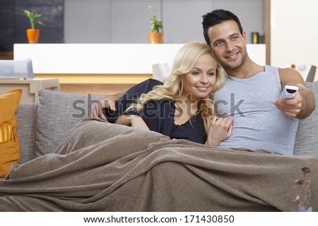 Attractive loving couple watching tv at home, smiling happy, sitting on sofa, embracing.