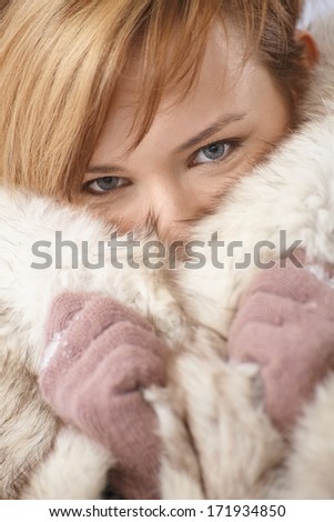 Portrait of beautiful young woman hiding her face in fur coat