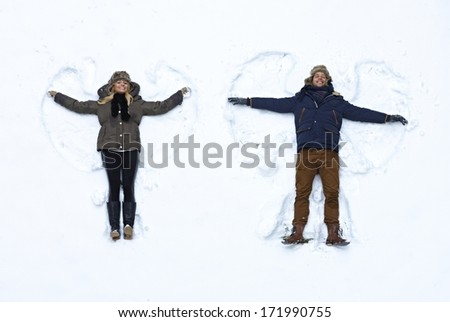 Young Couple Lying In Fresh Snow, Making Snow Angels Having Fun.