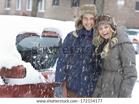 Happy Loving Couple Standing By Car, Drawing Heart In Snowfall, Smiling.