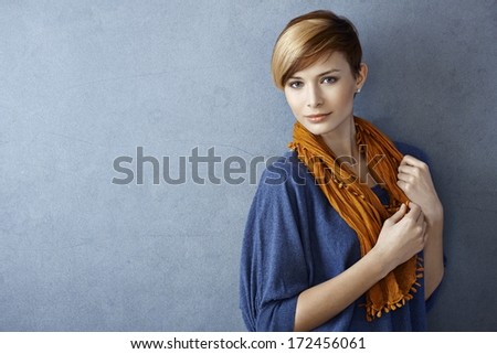 Beautiful young woman wearing scarf standing by grey wall, looking at camera. Copy space.