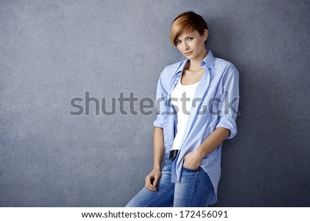 Casual young woman leaning to wall, hand in pocket