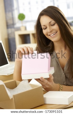 Happy young woman opening parcel, looking at gift box, smiling happy.