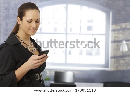 Young businesswoman using mobilephone, writing text message over window.