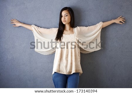 Attractive Asian girl posing by grey wall with arms wide open.