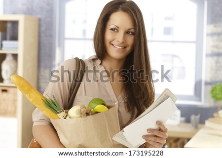 Happy woman arriving at home with shopping bag and mail, smiling.