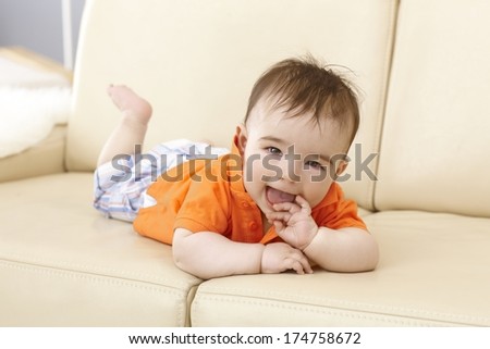 Beautiful baby boy lying on sofa, smiling happy with hand in mouth.