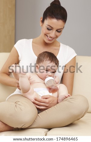 Happy mother holding naked little baby, feeding from feeding bottle.