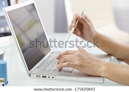 Closeup photo of male hands typing on laptop keyboard, holding pen.