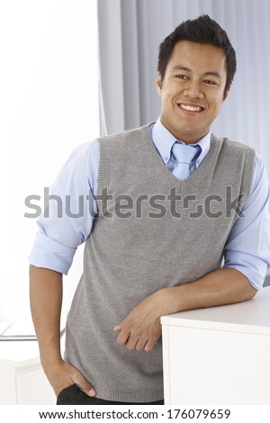 Portrait of happy young Asian man, smiling, looking away, leaning on counter.