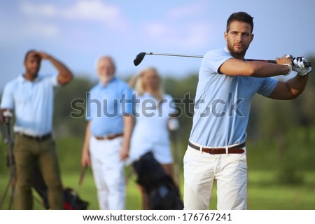 Handsome male golfer swinging golf club, following shot in the air.