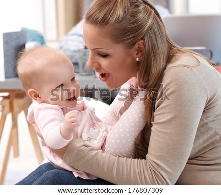 Young mother playing with little girl at home, both having fun.