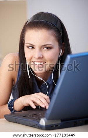 Happy schoolgirl listening music at home through headset on laptop.