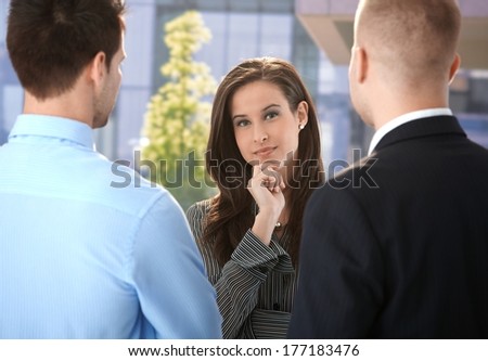Businesswoman listening to male colleagues, standing chatting outside of office building.