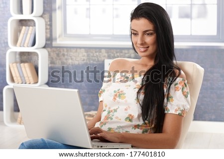 Attractive young female using laptop computer at home, browsing internet, smiling.