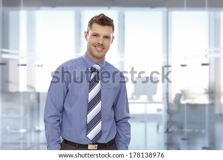 Portrait of happy young businessman at office, looking at camera, smiling. Copyspace.